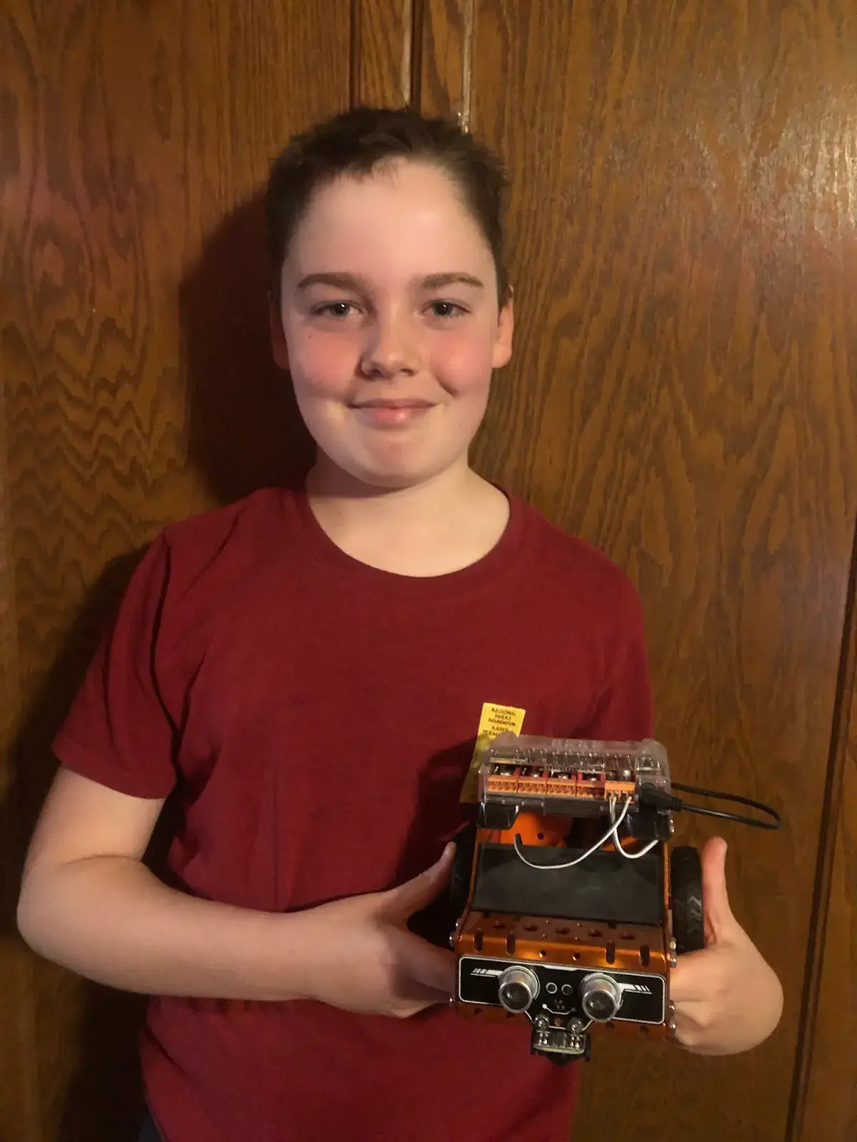 Student proudly holding the obstacle-avoiding rover he built in his ItsMyBot robotics classes